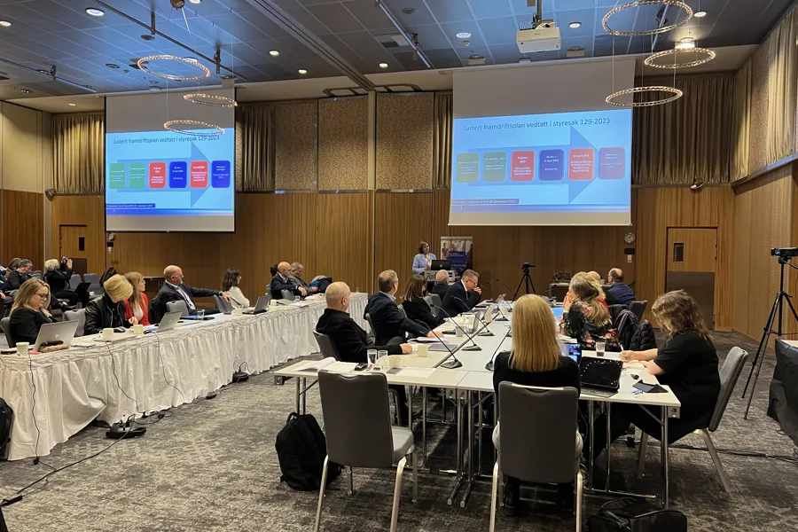 En gruppe mennesker som sitter ved langbord i et konferanserom