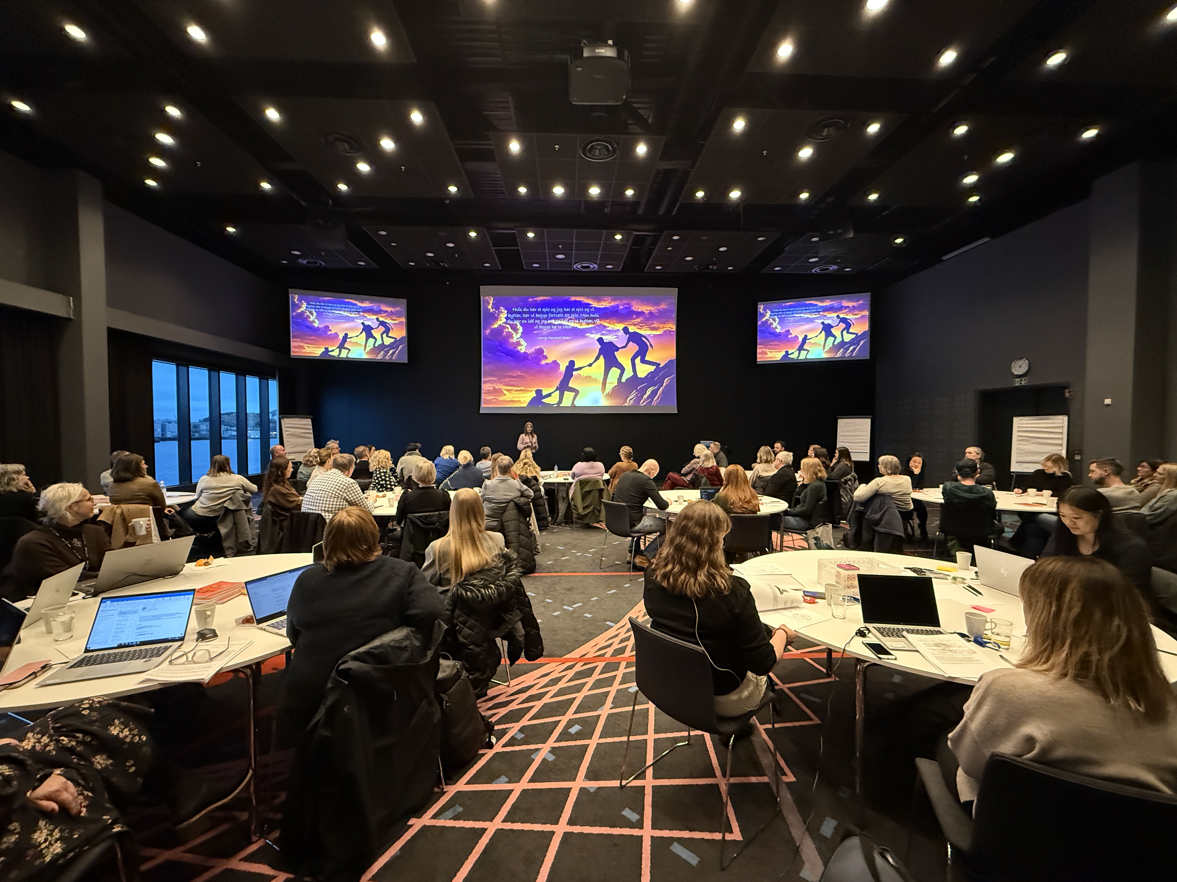 En gruppe mennesker som sitter i et rom med store skjermer