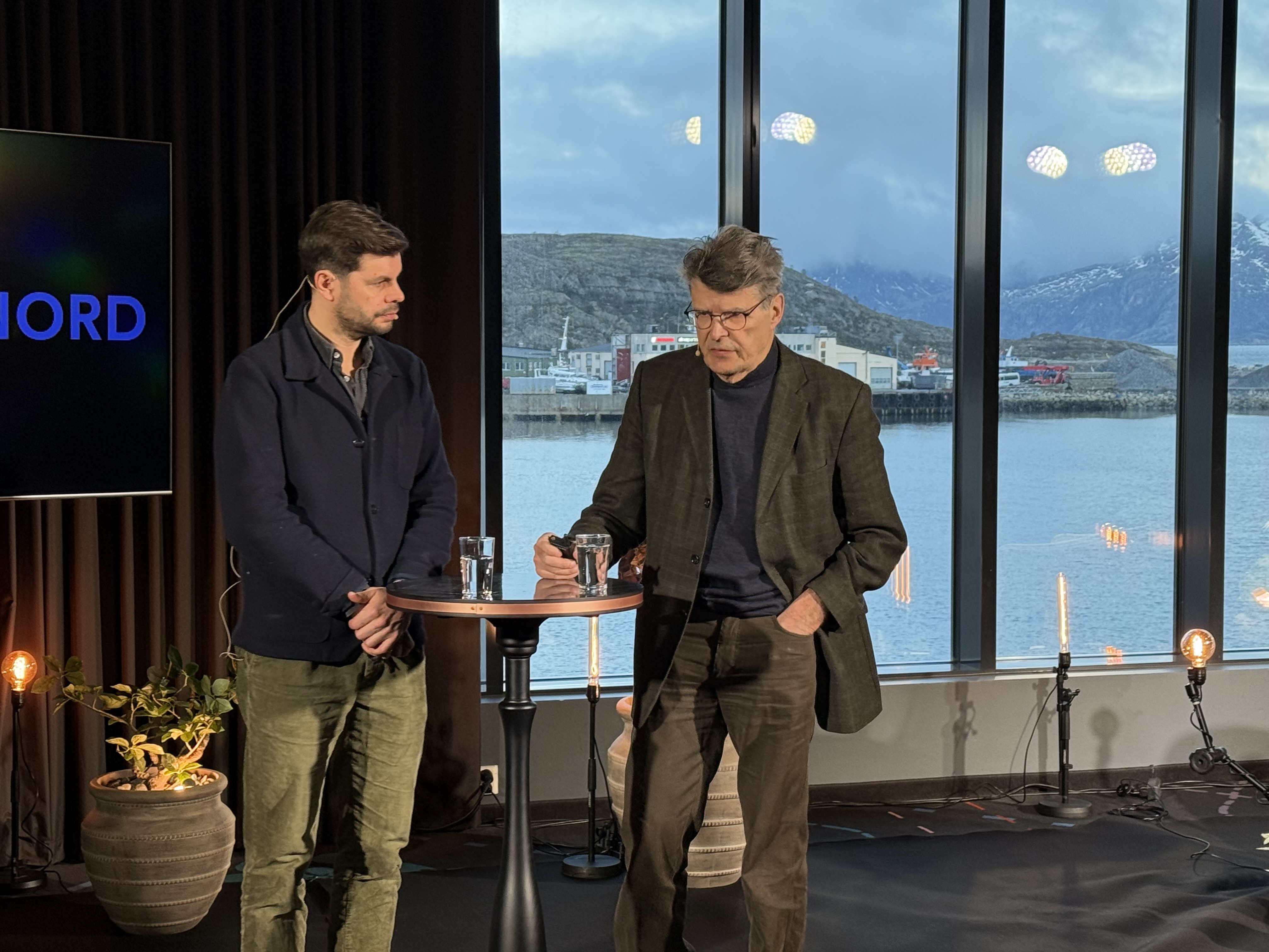 Et par menn som står foran et vindu med utsikt over en by