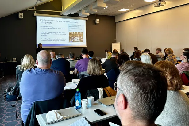 En gruppe mennesker som sitter i et rom og ser på en skjerm