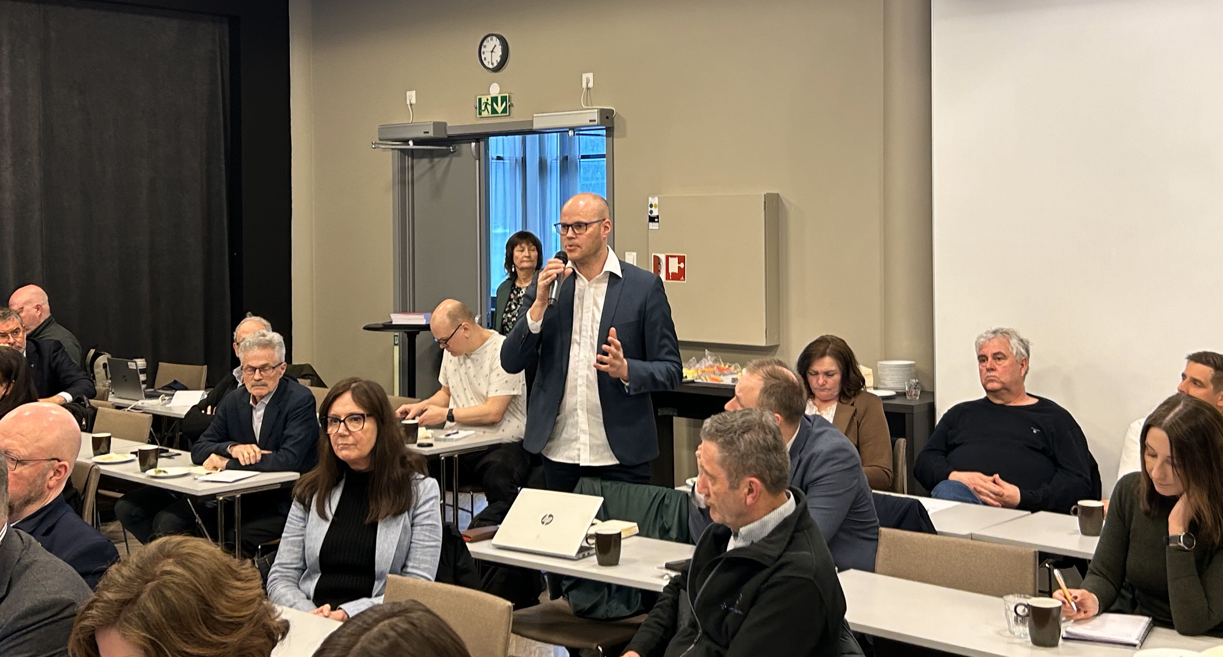 En person som snakker inn i en mikrofon foran en gruppe mennesker