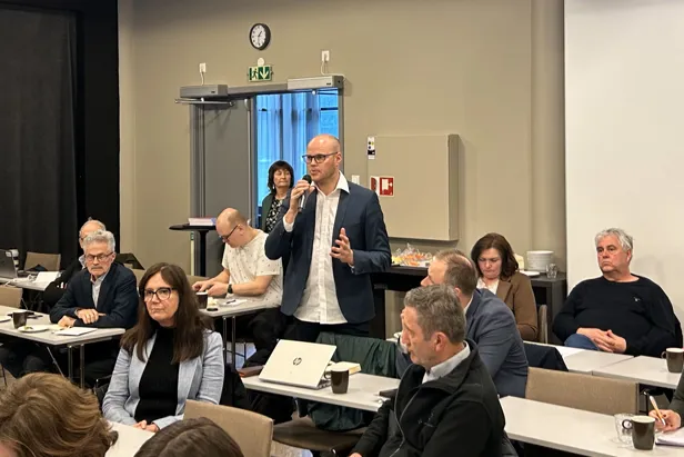 En person som snakker inn i en mikrofon foran en gruppe mennesker