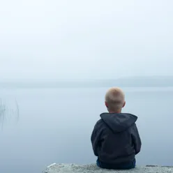 En mann som sitter på en stein og ser ut på vannet