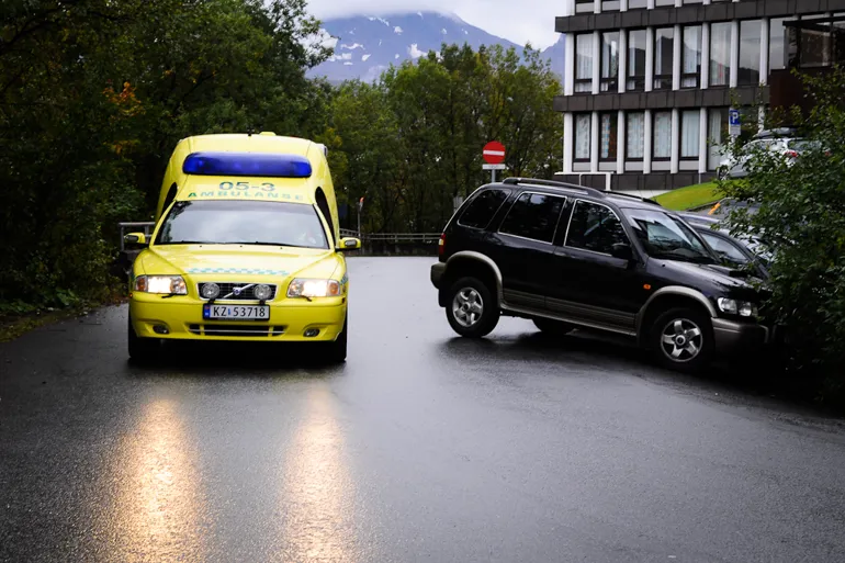 Et par biler parkert på en våt vei ved trær og bygninger