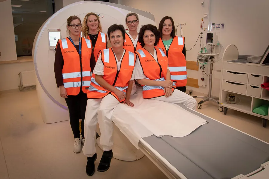 En gruppe mennesker i oransje vester som står ved siden av en seng