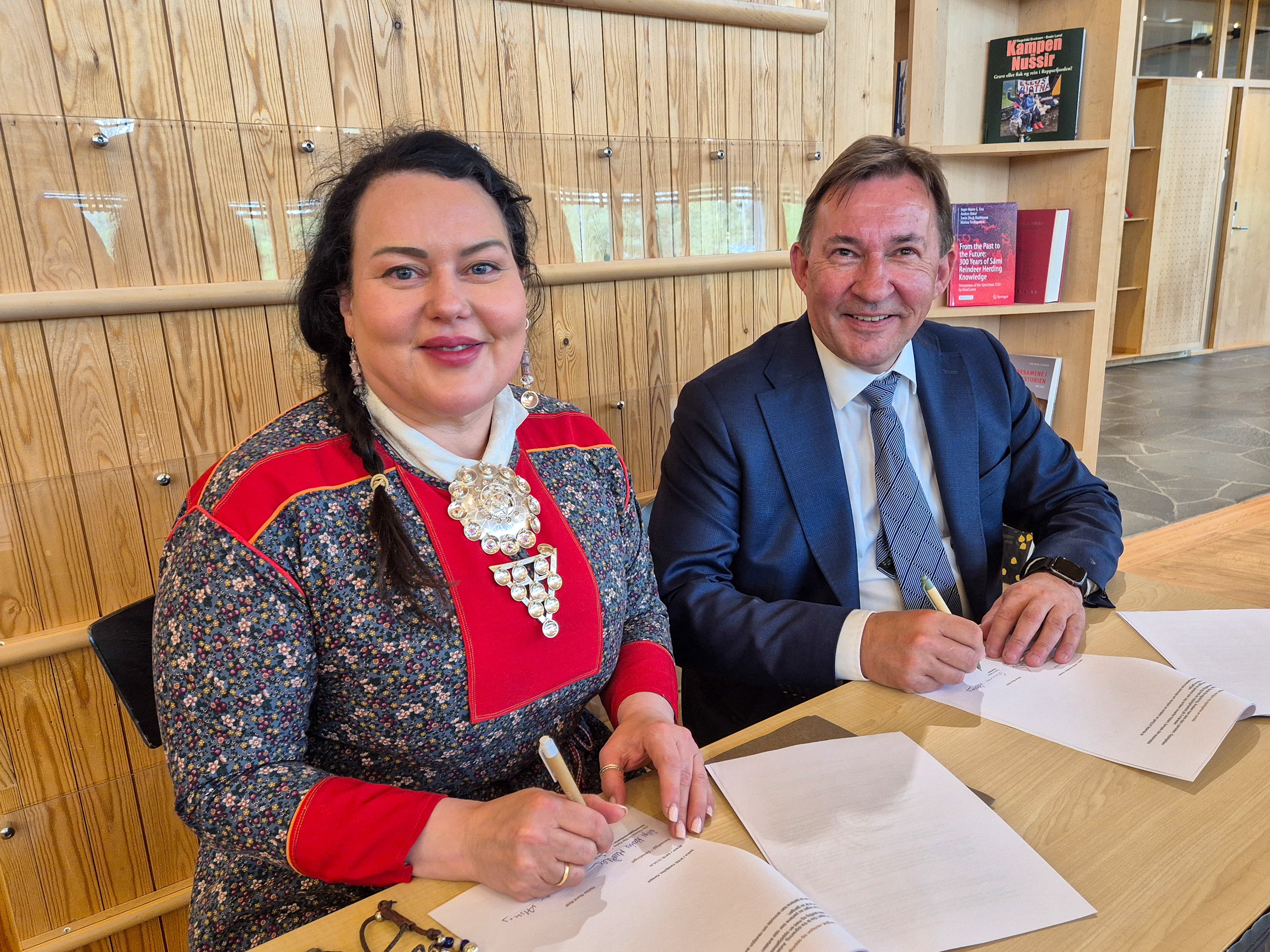Kvinne i kofte og mann i dress signerer papirer