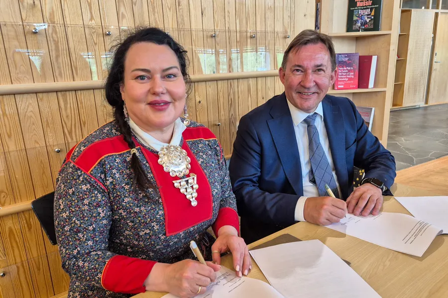 Kvinne i kofte og mann i dress signerer papirer