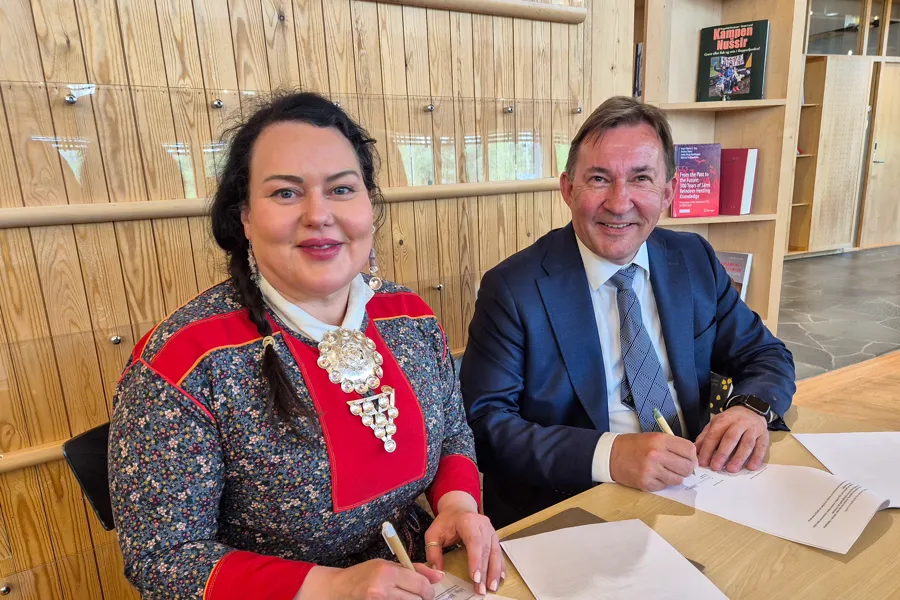 Kvinne i kofte og mann i dress signerer papirer