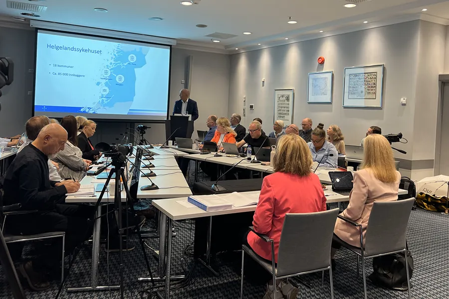 En gruppe mennesker som sitter ved et bord med en projektorskjerm