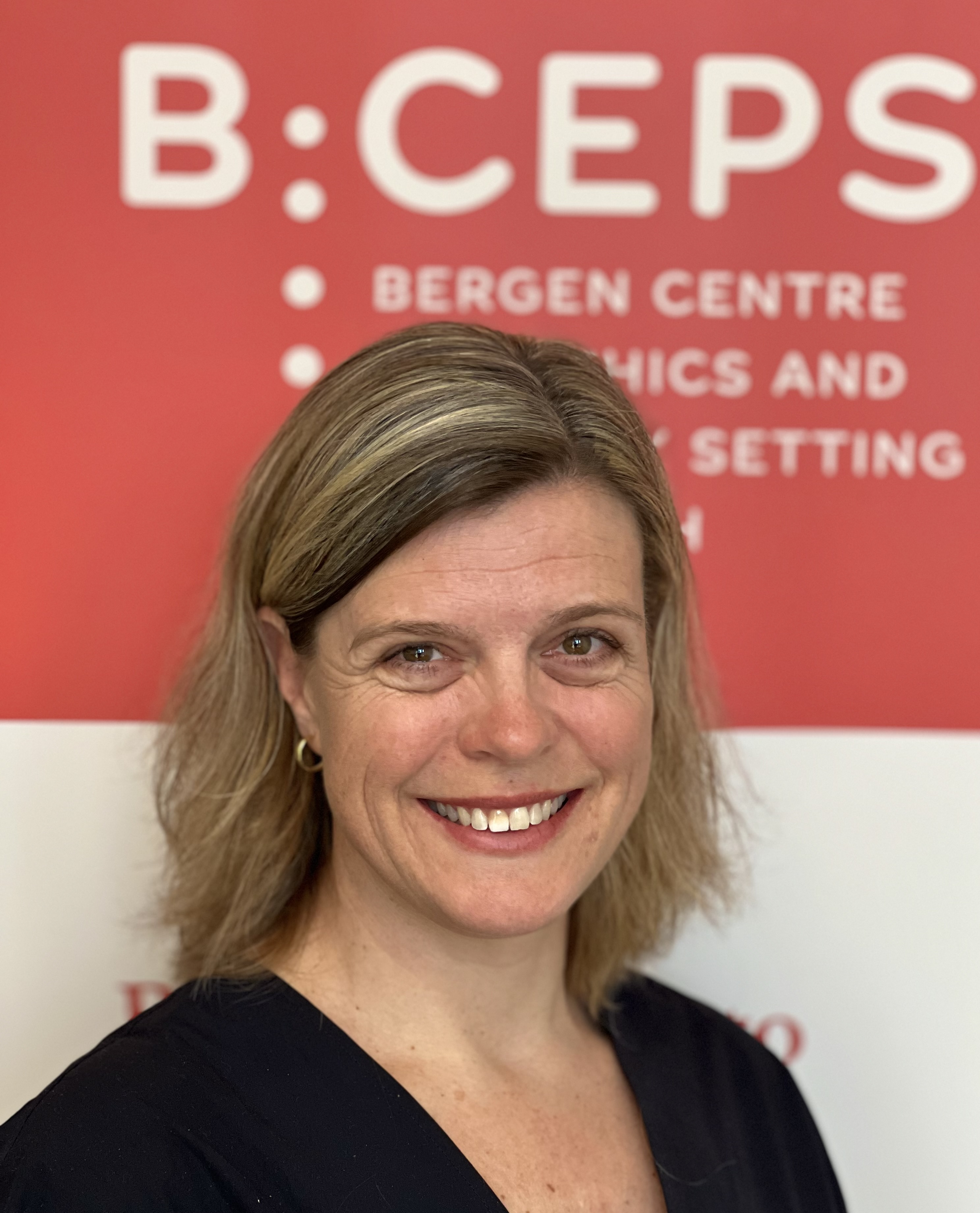 En person som smiler foran et rødt skilt