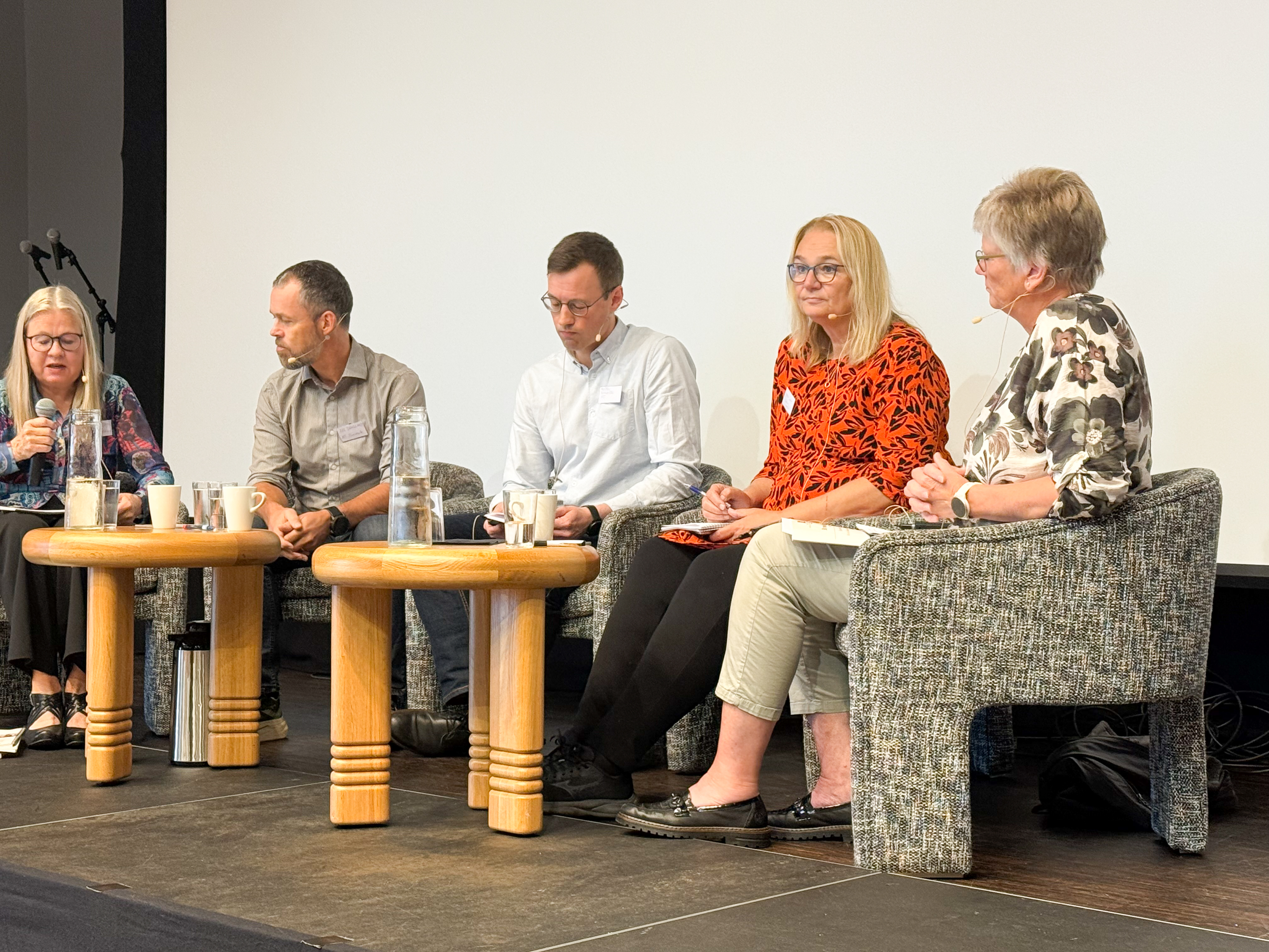 Fem mennesker på en scene sittende i stoler