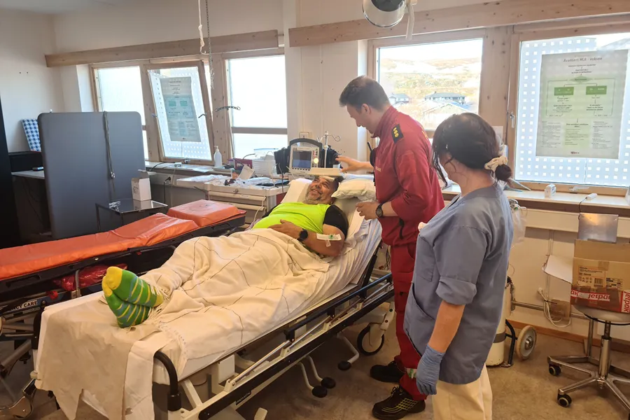 Pasient i seng som snakker med helsepersonell