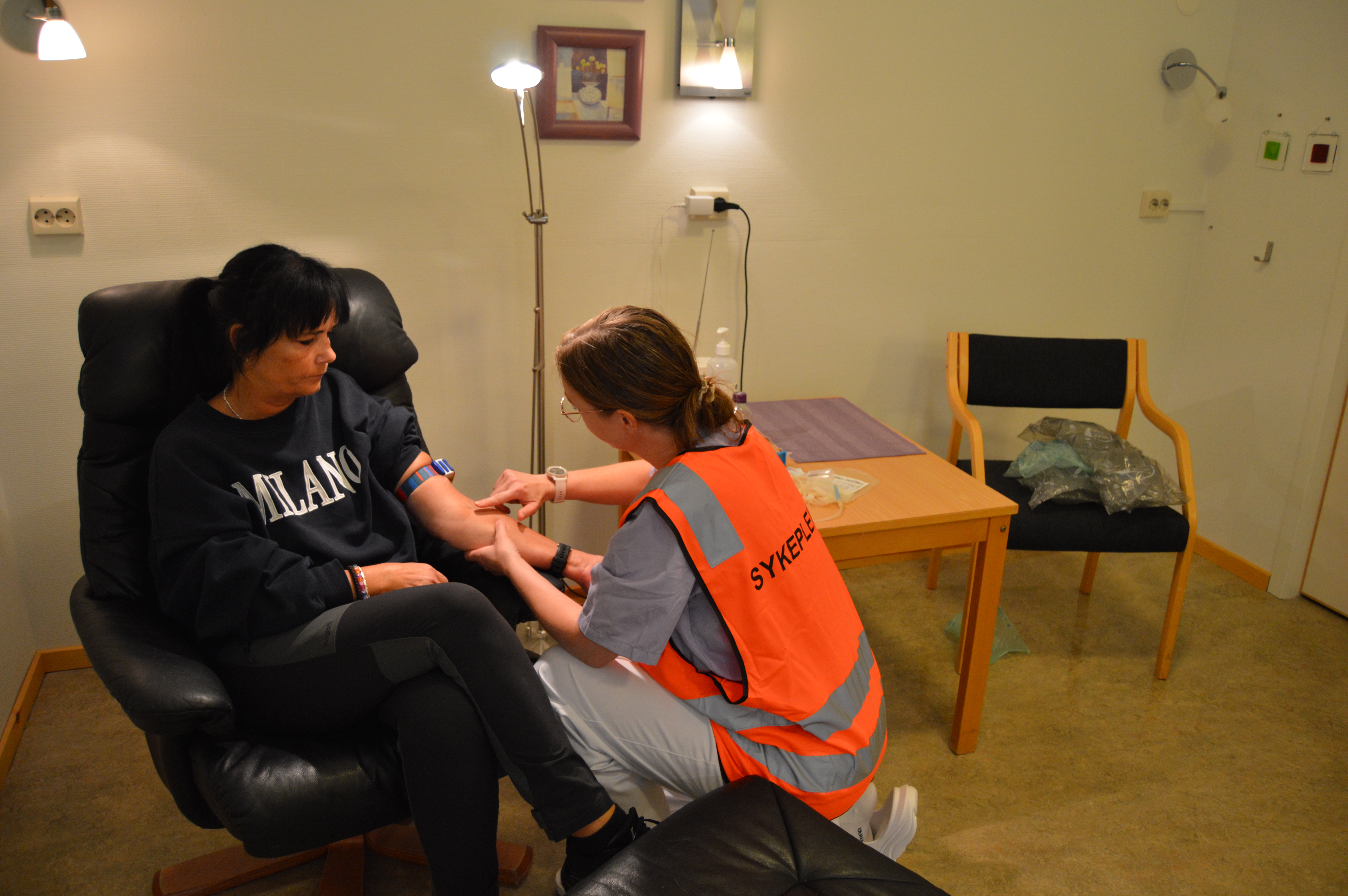 Person sittende i stol tappes for blod av helsepersonell