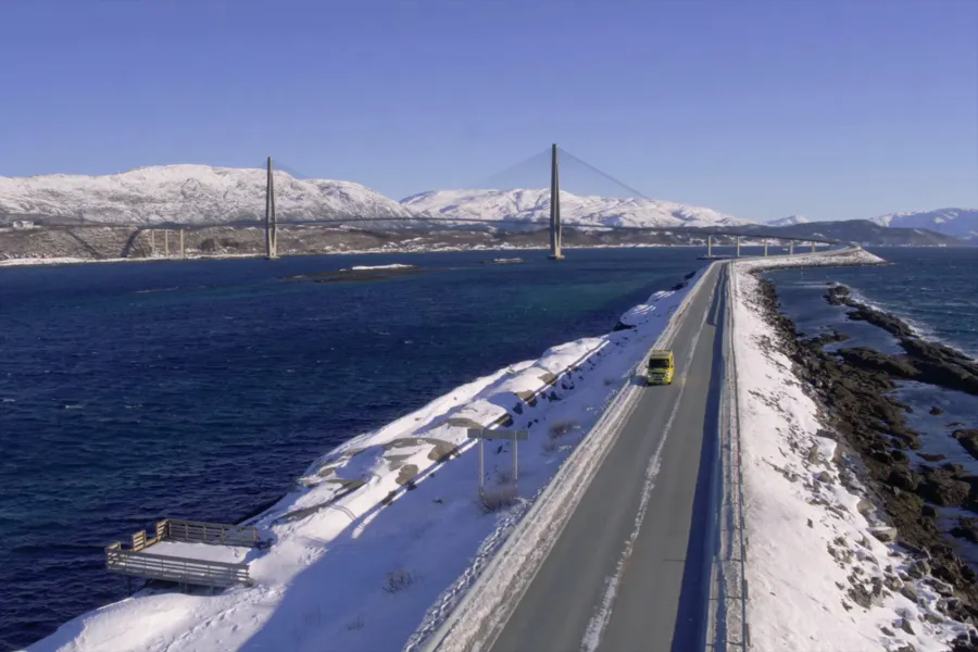 En ambulanse kjører over en lang bro over en vannmasse med snø på sidene