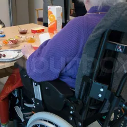 En person som sitter ved et bord med rullestol og et bord med mat