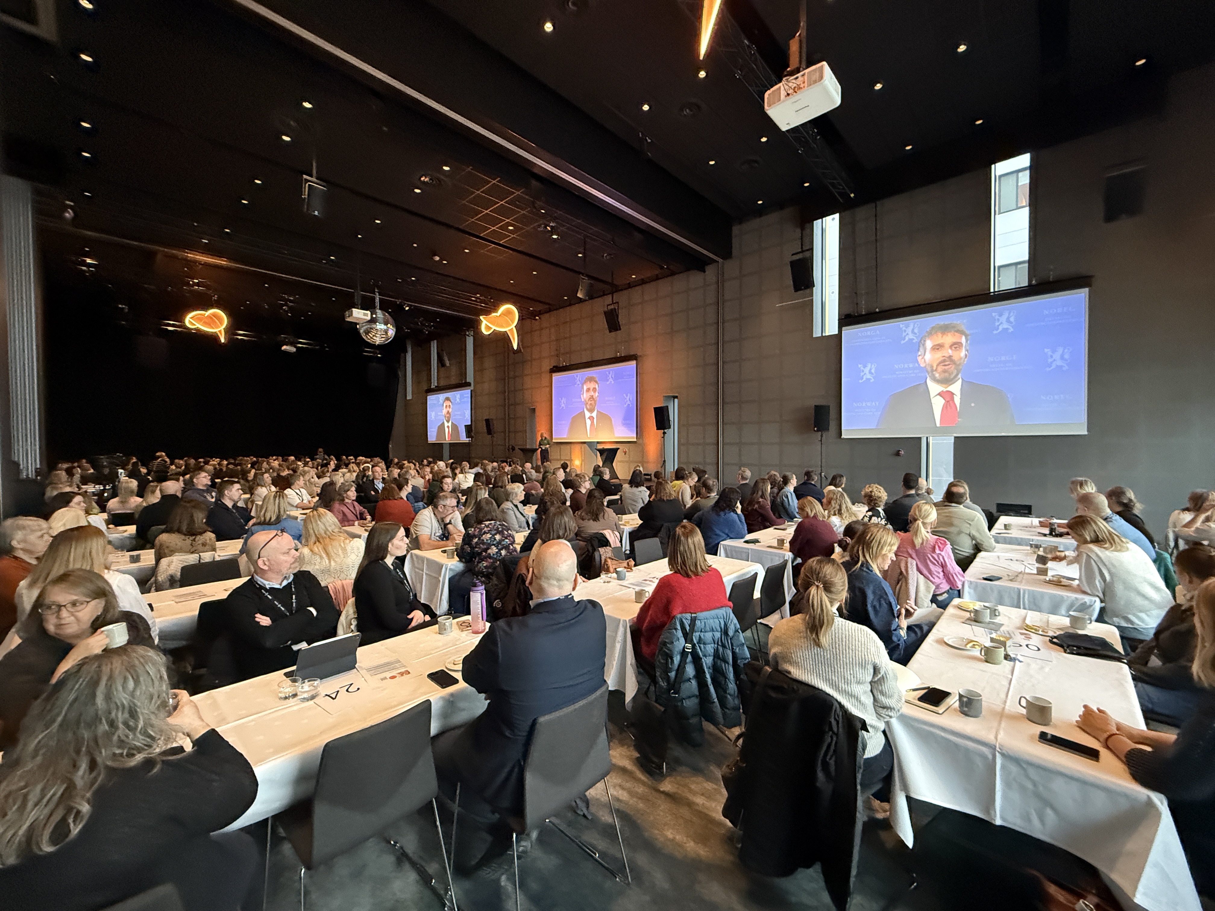 En gruppe mennesker som sitter ved bord og ser på en presentasjon