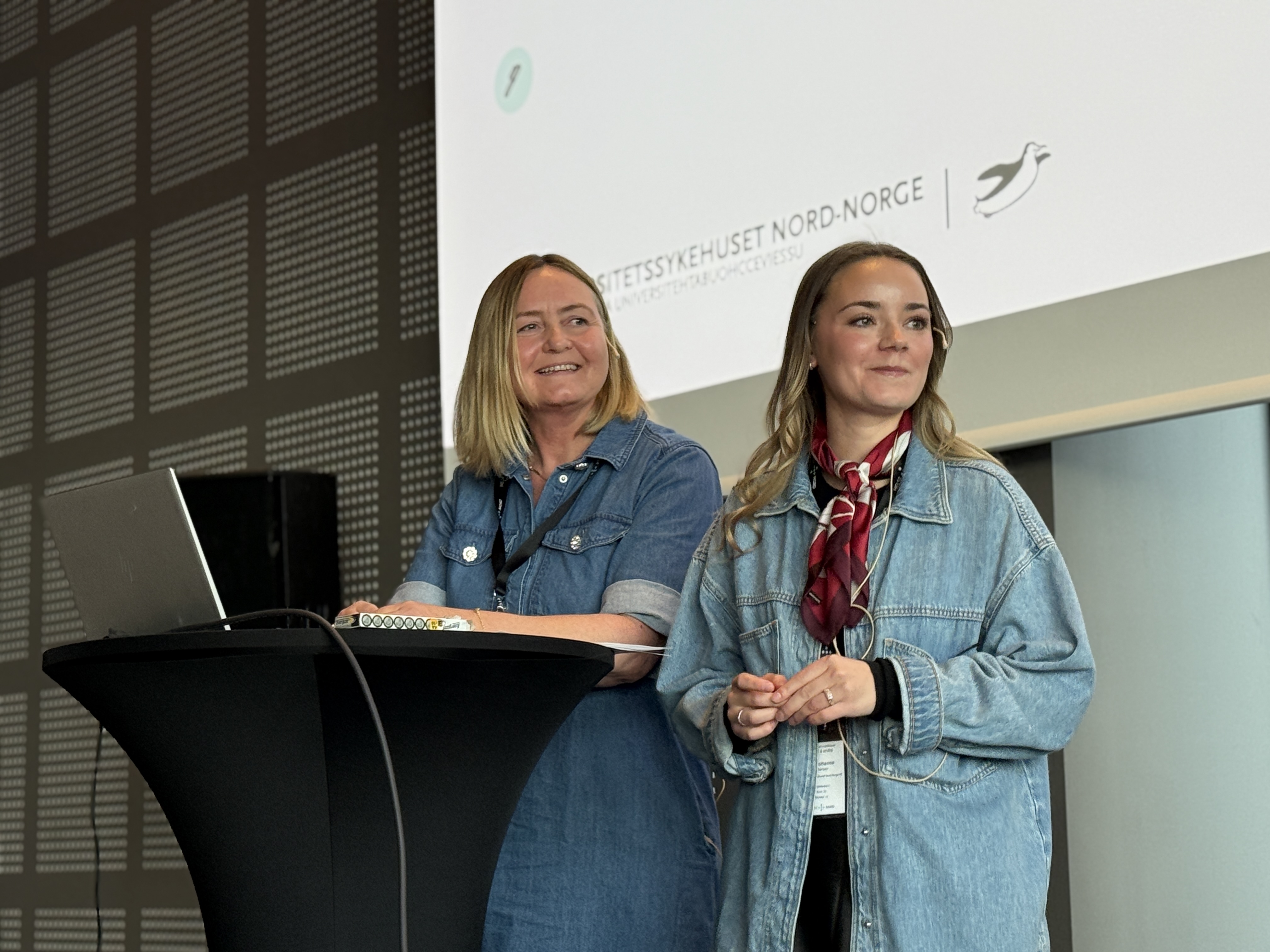 Kvinner i blå jakker som står foran en datamaskin