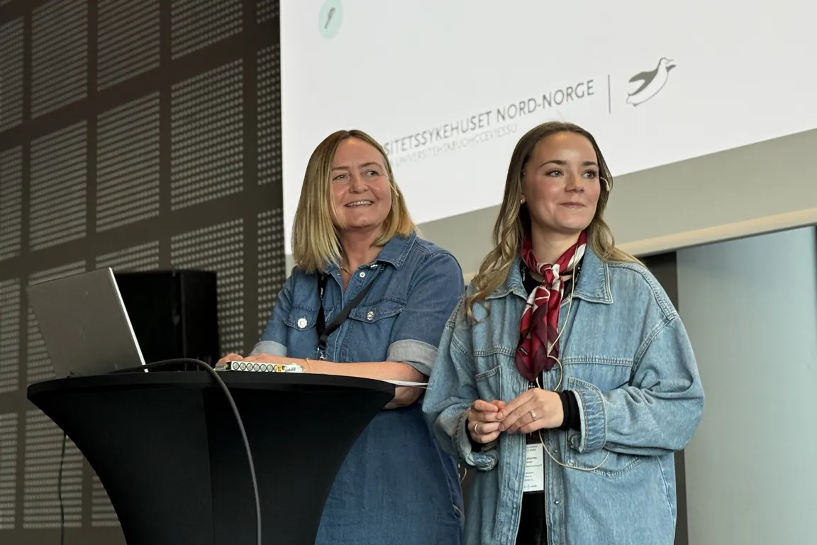 Kvinner i blå jakker som står foran en datamaskin