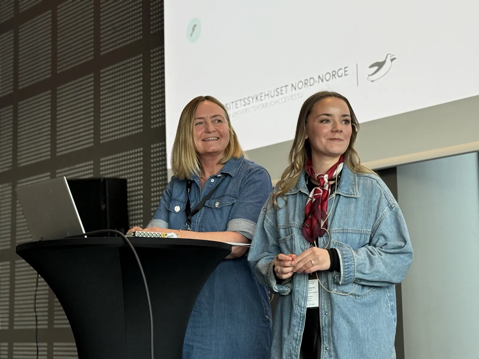 Kvinner i blå jakker som står foran en datamaskin