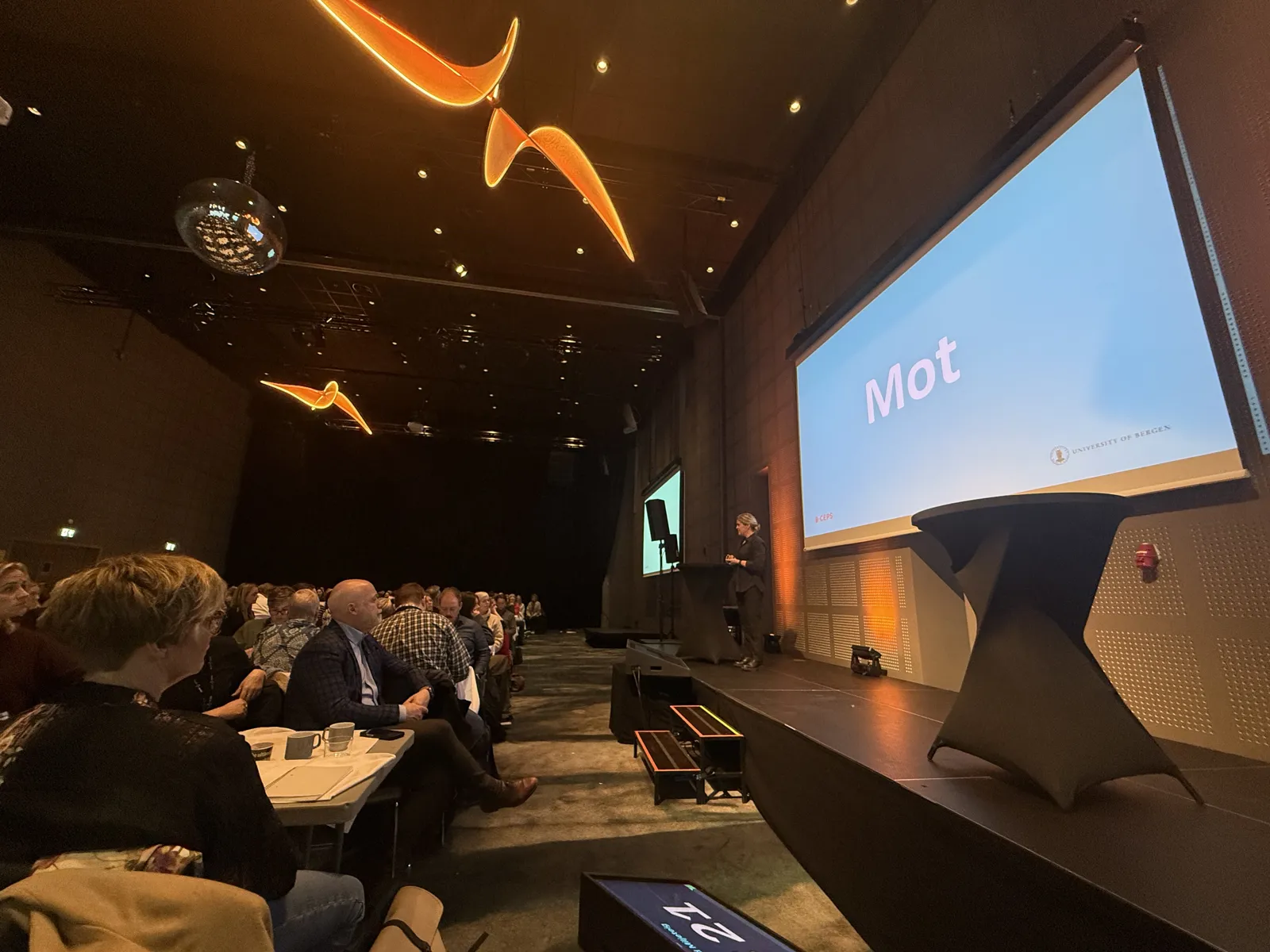 En gruppe mennesker som sitter i et rom med en stor skjerm