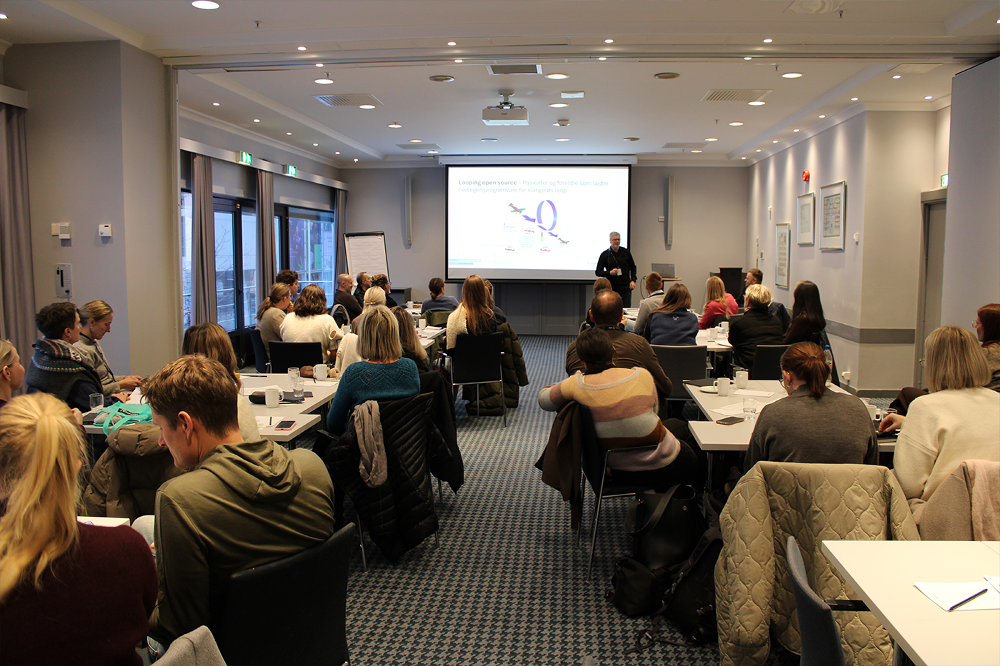 En gruppe mennesker som sitter i et rom og ser på en skjerm