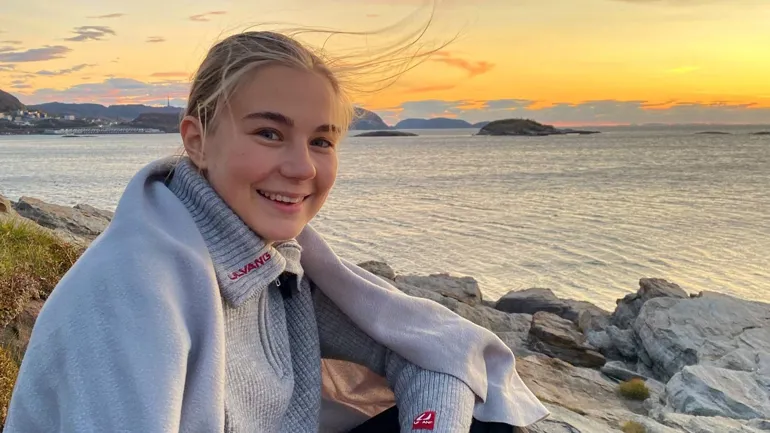 En person som sitter på en stein med en drink og en vannmasse i bakgrunnen