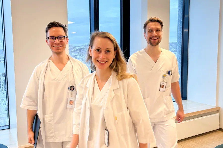 En gruppe mennesker iført hvite laboratoriefrakker og står foran et vindu