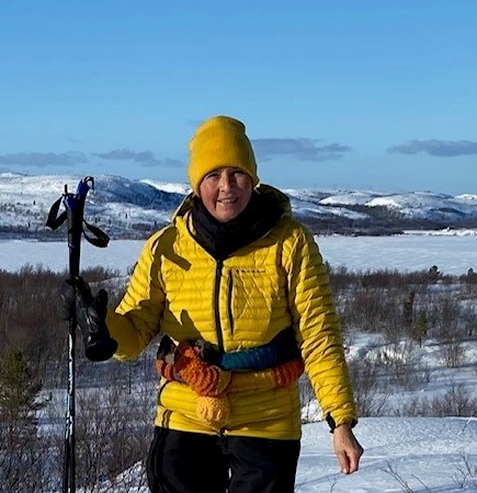 En mann iført en gul jakke og holder et par skistaver