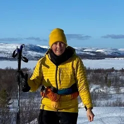 En mann iført en gul jakke og holder et par skistaver