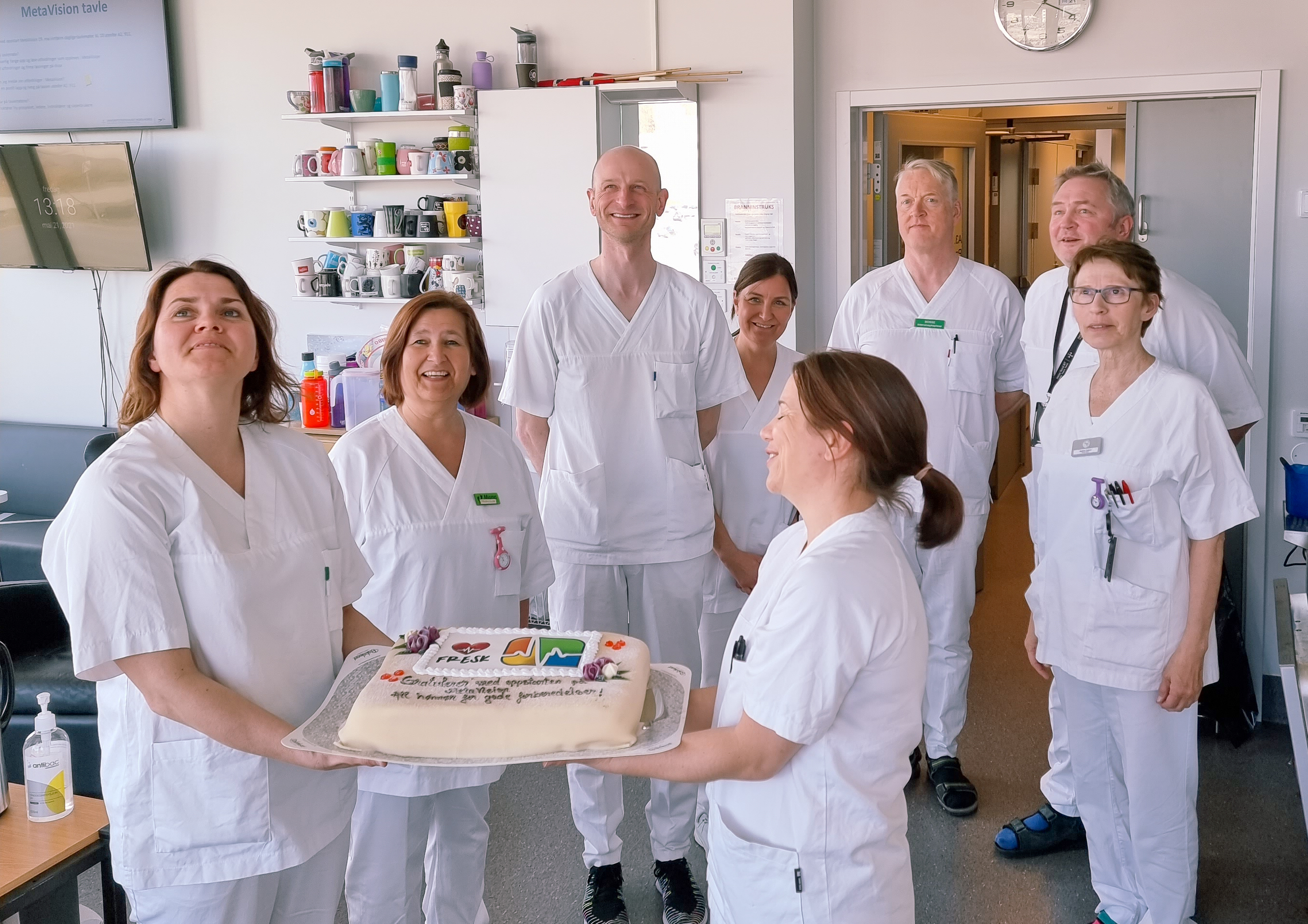 En gruppe mennesker i hvite laboratoriefrakker som holder en kake